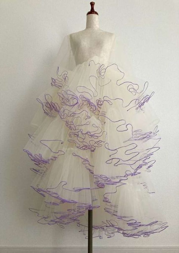 Alt Text: “Avant-garde cream tulle dress with layered volume and abstract purple thread detailing, displayed on a mannequin.”