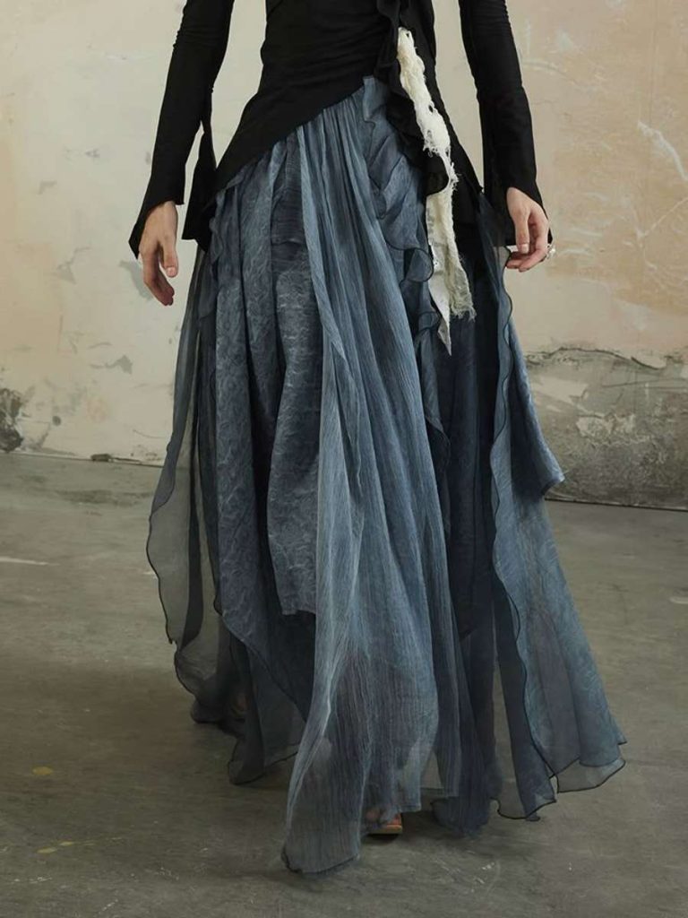 “Model wearing a flowing, layered sheer blue maxi skirt paired with a fitted black top — runway-inspired dramatic skirt trend for SS26.”