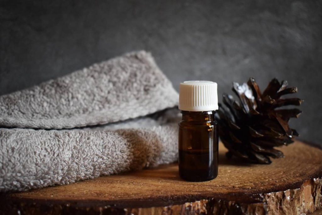 Alt Text: Brown essential oil bottle with pine cone and towel on wooden surface.