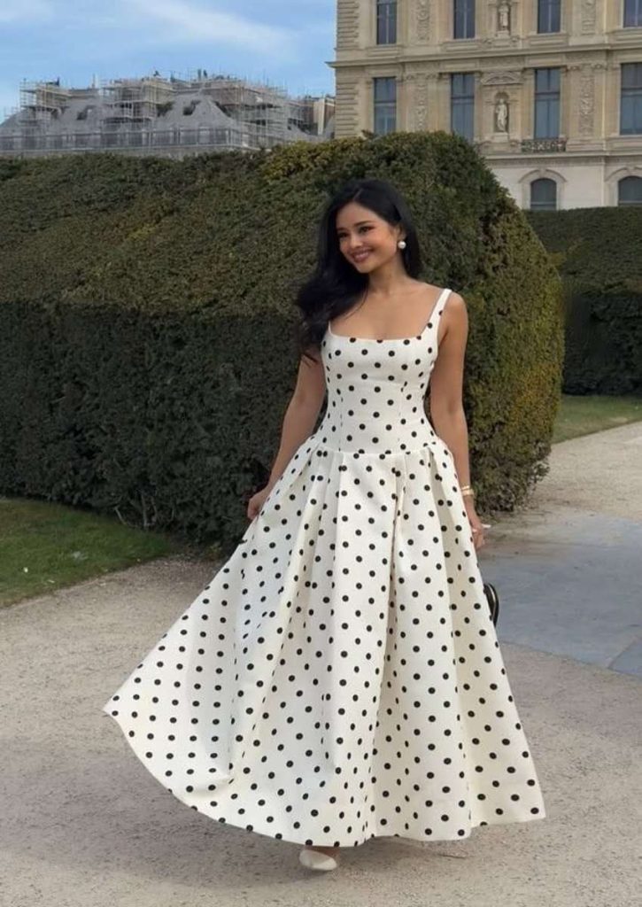 “Woman wearing a sleeveless white maxi dress with black polka dots, styled elegantly outdoors with a flowing silhouette.”