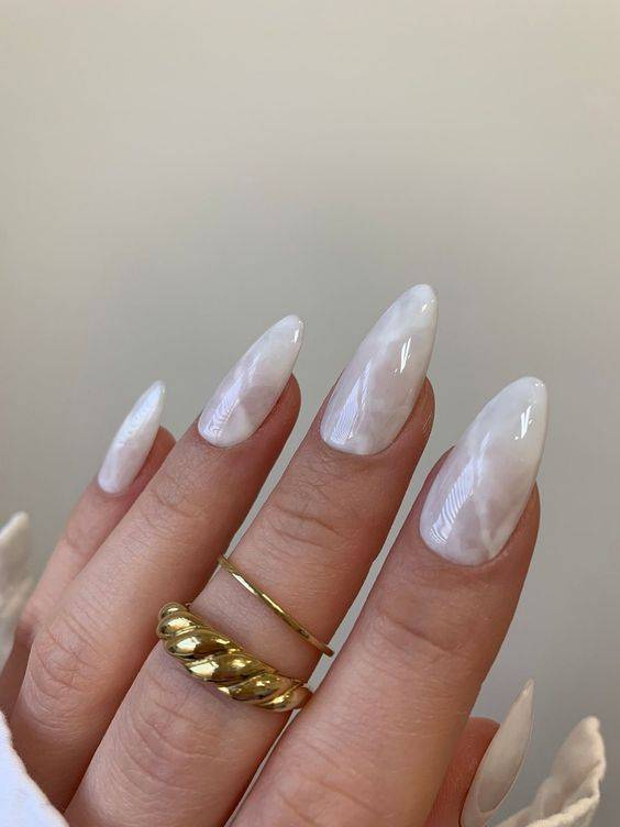 White marble ombre nails with glossy finish, close-up of hand wearing gold rings.