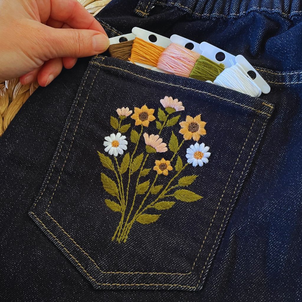 Hands embroidering floral patterns on denim, representing creative DIY embroidery fashion.