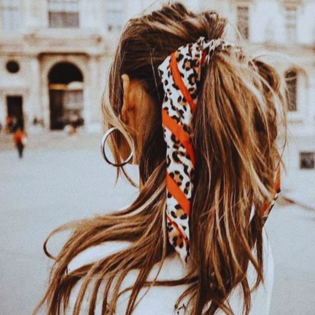 Model tying a polka dot scarf around her ponytail, soft daylight setting — relaxed feminine style.