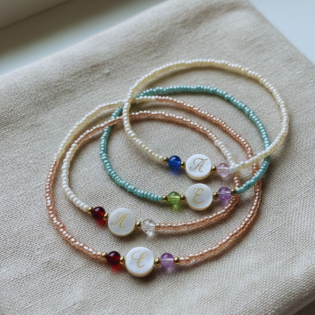 Beaded bracelets with birthstones and letter charms on a fabric background.