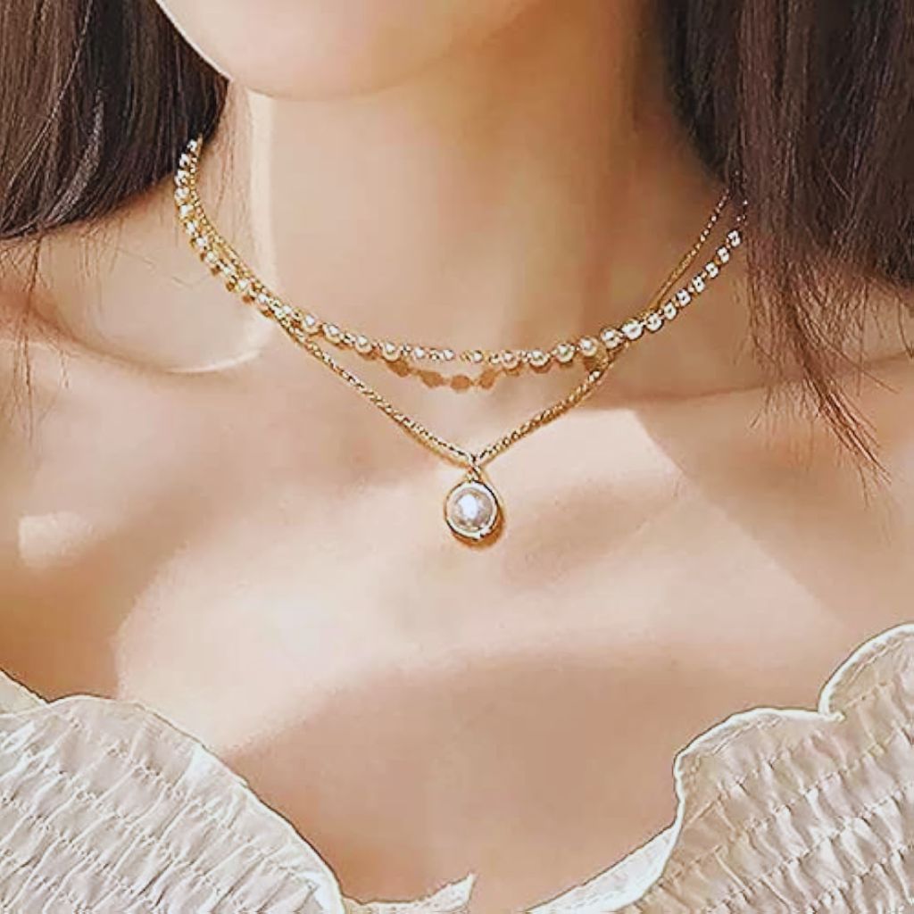 Flat lay of gold and pearl necklaces with mixed textures — thin chains, beads, and pendants — arranged to show how to layer different necklace styles together.