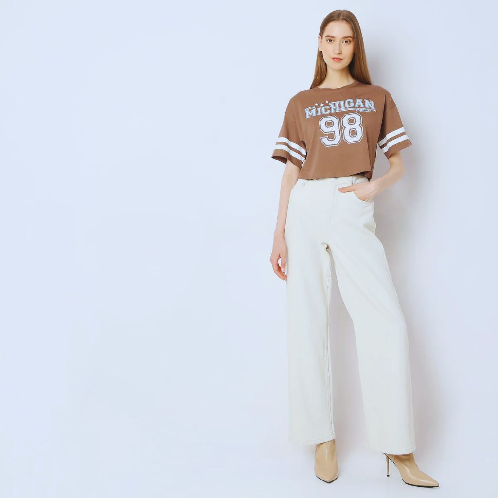 Model wearing a boxy cropped oversized T-shirt tucked into tailored trousers with minimalist sneakers, clean modern outfit aesthetic.