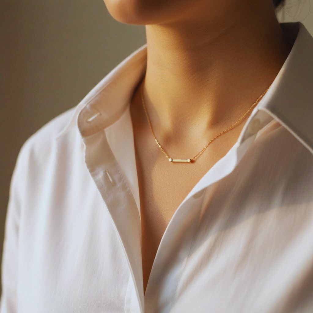 Close-up of a delicate gold chain necklace with a minimalist pendant styled over a white shirt.
