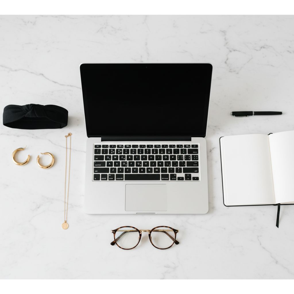 “Flat-lay of minimalist gold jewelry, headband, and blue-light glasses next to a laptop, symbolizing simple and elegant Zoom-ready accessories.”