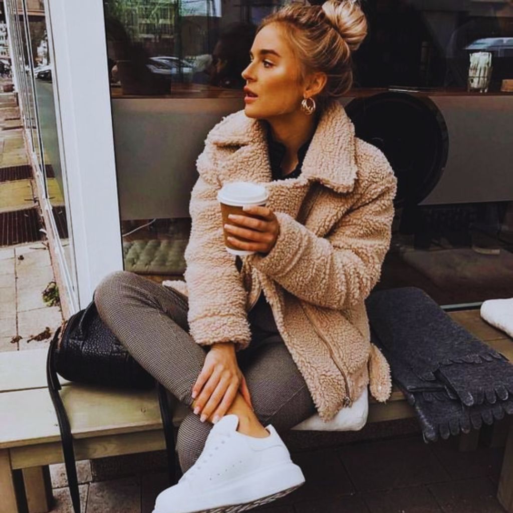 "Woman in oversized beige teddy coat with jeans and Chelsea boots holding coffee outdoors."
