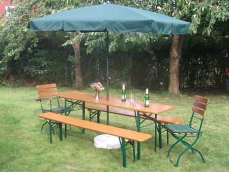 Traditional beer garden setup with wooden benches, a long table, and a green umbrella in a backyard setting.
