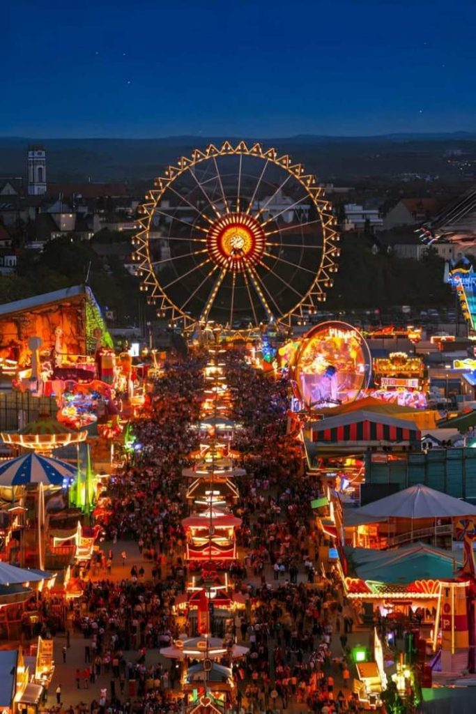 Aerial night view of Oktoberfest with a brightly lit Ferris wheel and crowded festive streets