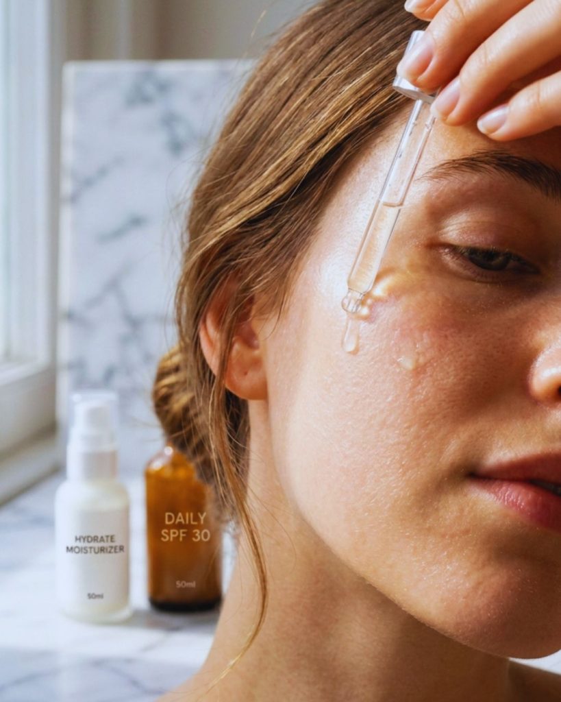 Close-up of vitamin C serum being applied to skin in bright morning light.