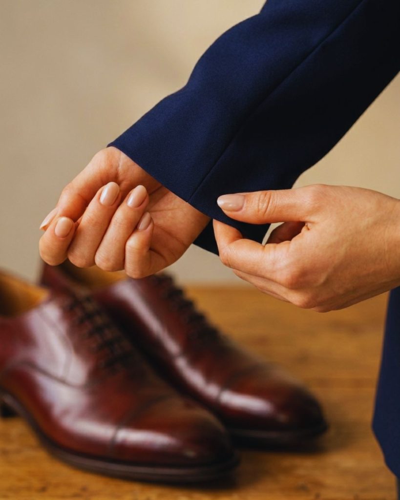 Close-up of polished shoes, clean cuff, and manicured hands signaling attention to detail.