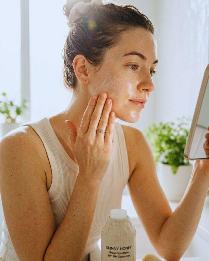Woman applying sunscreen to face and neck in bright natural light.