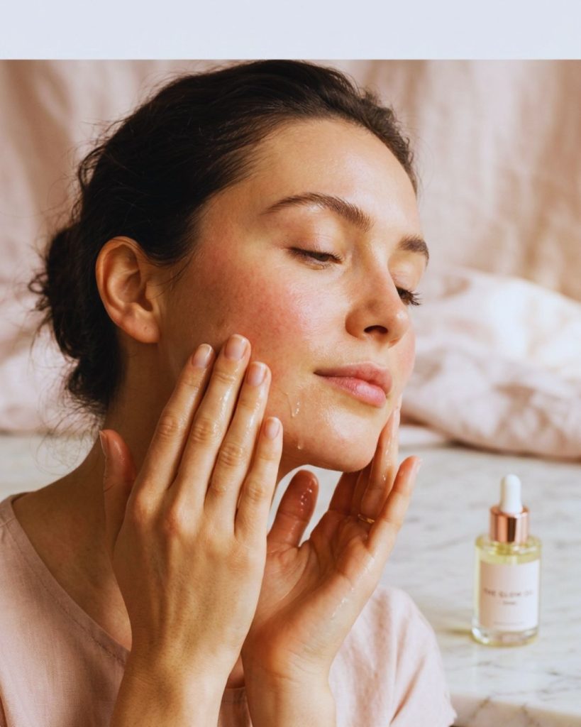 Woman massaging her face with facial oil using upward strokes to improve circulation and reduce puffiness.