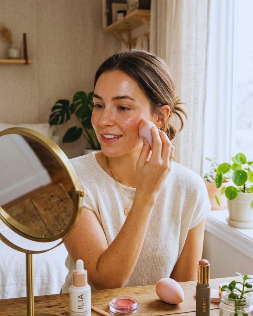 Woman applying lightweight skin tint and cream blush for a natural clean girl makeup look with glowing skin.