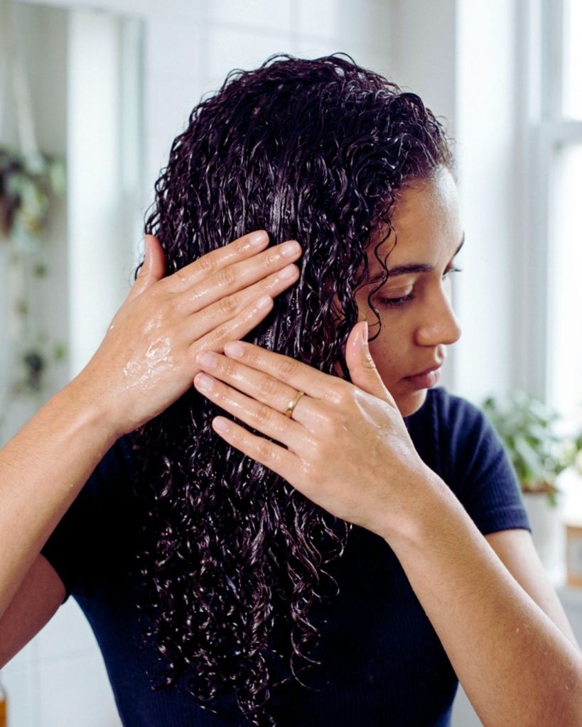 Applying gel to wet curly hair using praying hands technique and scrunching for curl definition.